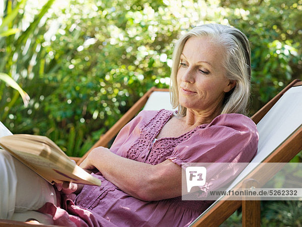 Frau sitzt auf Liegestuhl im Garten mit Buch