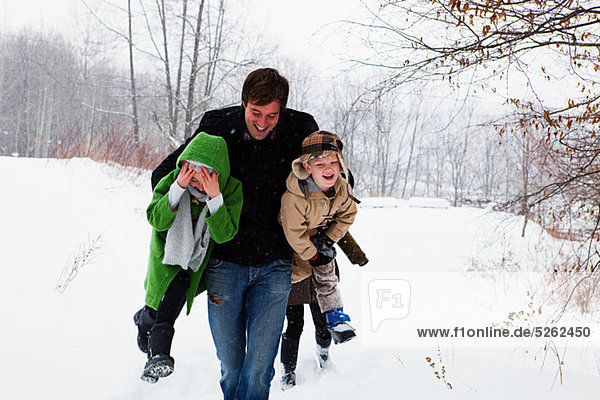 Father carrying son and daughter in snow