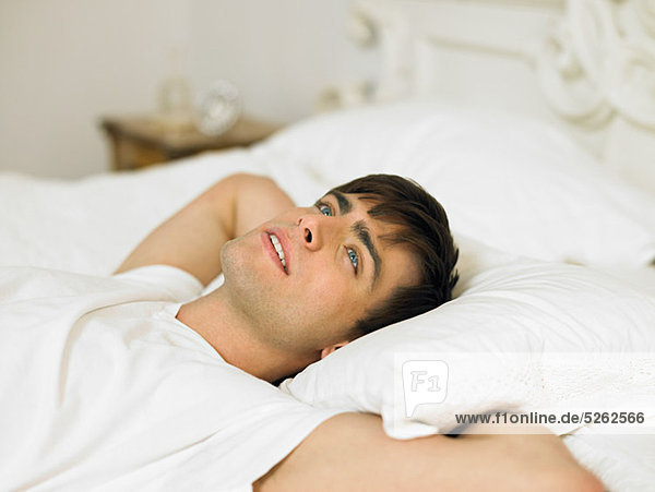 Junger Mann liegt auf dem Bett mit den Händen hinter dem Kopf