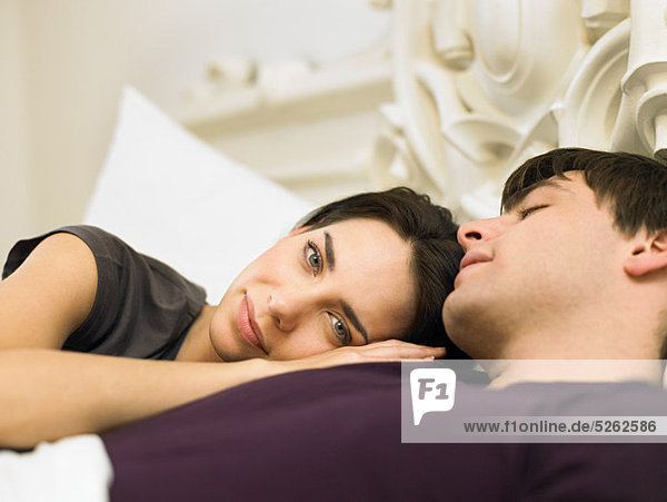 Young couple lying in bed  woman's head on man's shoulder