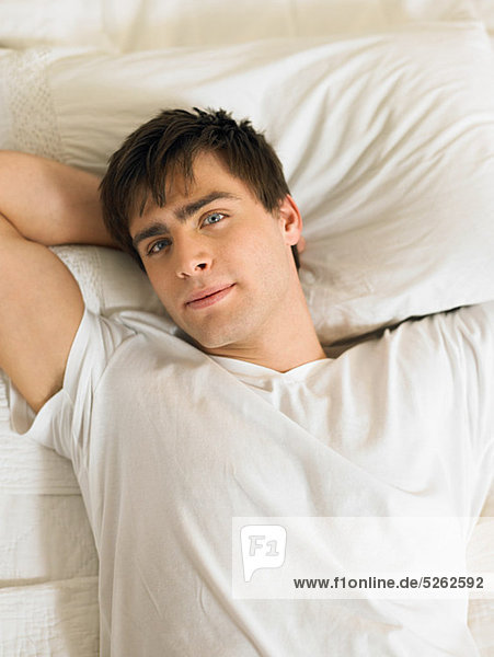 Young man lying on bed with hands behind head  portrait