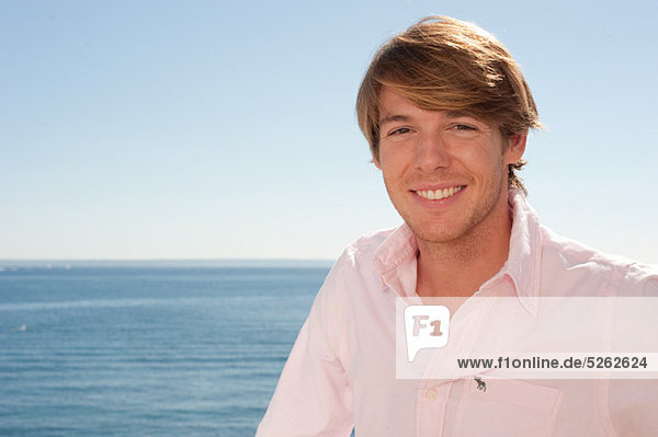 Young man in pink shirt by the ocean