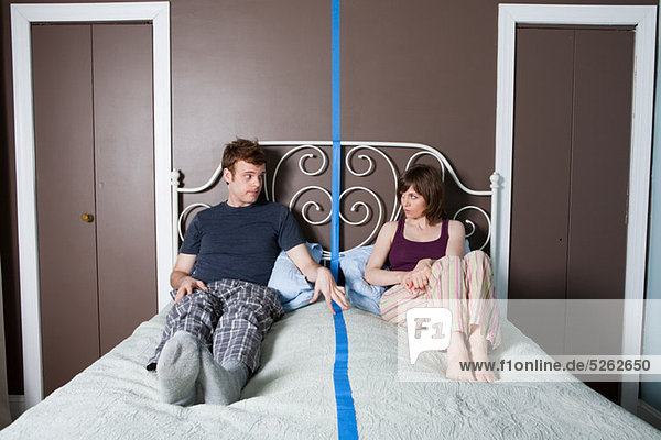 Young couple sitting on bed separated by blue line