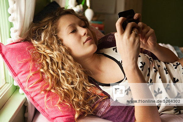 Teenage girl lying on bed with smartphone