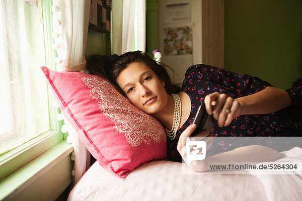 Teenagermädchen auf dem Bett liegend mit Smartphone