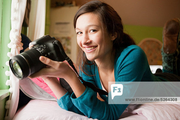 Teenage girl lying on bed with camera  portrait