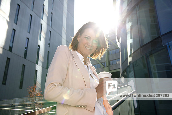 Lächelnde Geschäftsfrau mit Coffee to Go im Freien