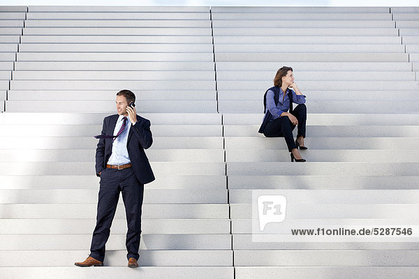 Geschäftsfrau und telefonierender Geschäftsmann auf einer Treppe