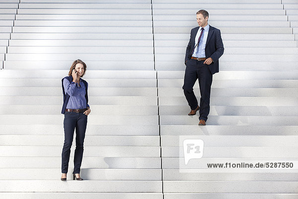 Geschäftsmann schaut auf telefonierende Geschäftsfrau auf einer Treppe