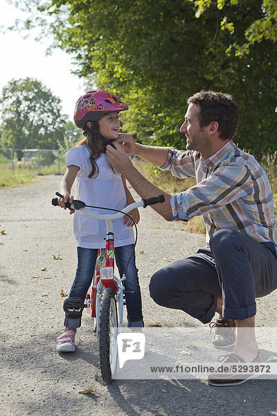 Vater schließt den Helm seiner Tochter auf dem Fahrrad