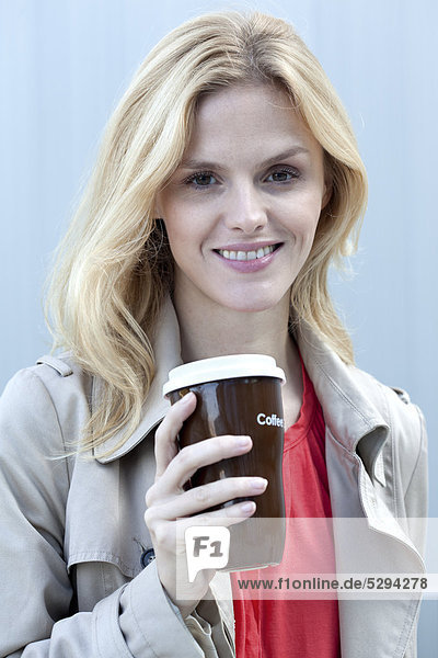 Lächelnde blonde Frau mit Coffee to Go