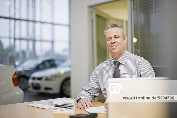 Car salesman sitting at desk in showroom