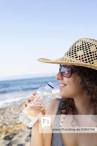 Lächelnde Frau trinkt Wasser am Strand