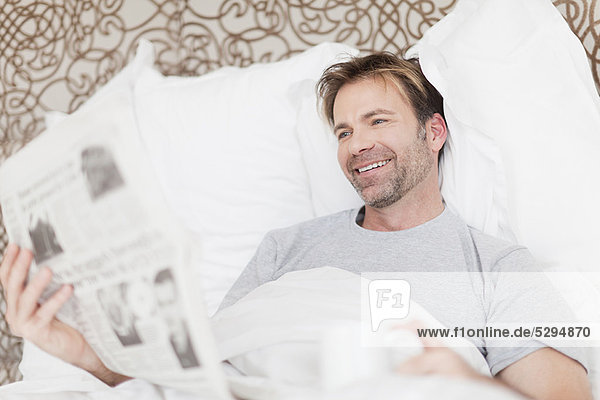 Mann  lächeln  Bett  Zeitung  vorlesen