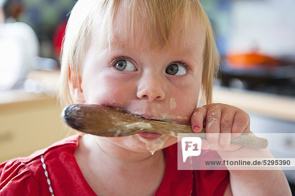 Toddler girl licking wooden spoon