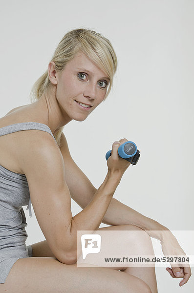 Young woman sitting and holding a small dumbbell in her right hand