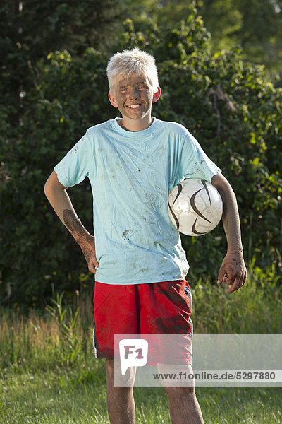 Portrait of a dirty  smiling boy with a football under his arm
