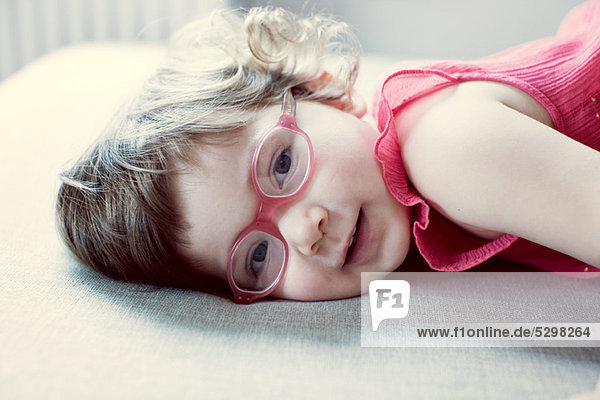 Kleines Mädchen mit Brille auf der Seite liegend