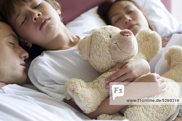 Junge schläft mit seinen Eltern im Bett  hält Teddybär in der Hand