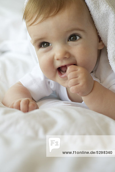 Baby auf Decke liegend  Daumen in den Mund steckend  Portrait