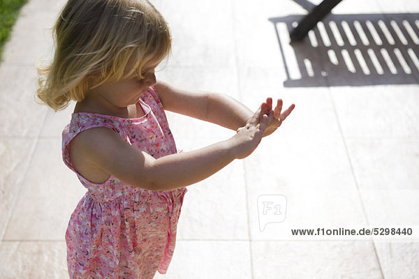 Kleines Mädchen  das im Freien steht und die Hände betrachtet.