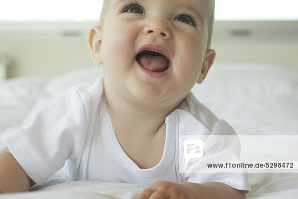 Baby lying on bed  looking up with open mouth