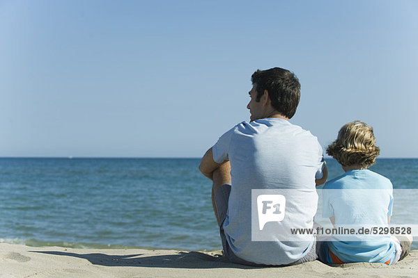 Vater und Sohn sitzen zusammen am Strand  Rückansicht