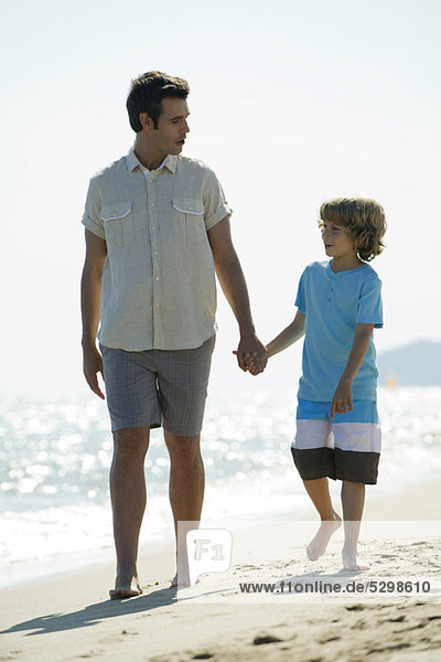 Vater und Sohn gehen Hand in Hand am Strand.