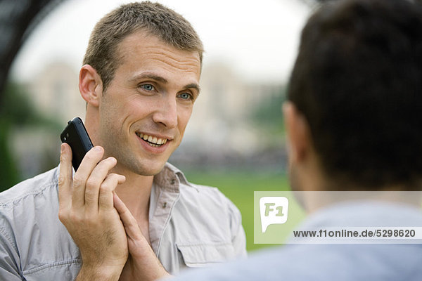 Mann am Telefon  der das Handy-Mundstück mit der Hand bedeckt  um mit Bekannten zu sprechen.