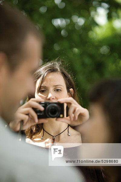 Woman photographing couple with digital camera  over the shoulder view