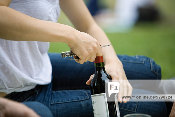 Frau entkorkt Flasche Wein im Freien  abgeschnitten