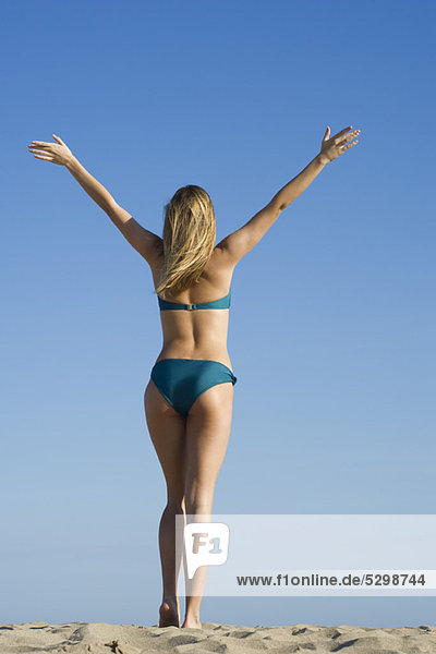 Woman at the beach with arms raised in air  rear view