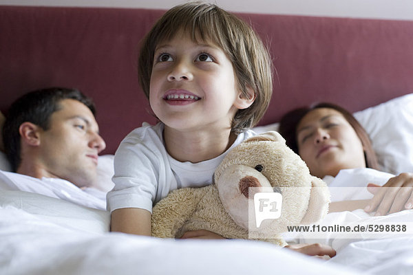 Junge im Bett der Eltern sitzend  Teddybär umarmend