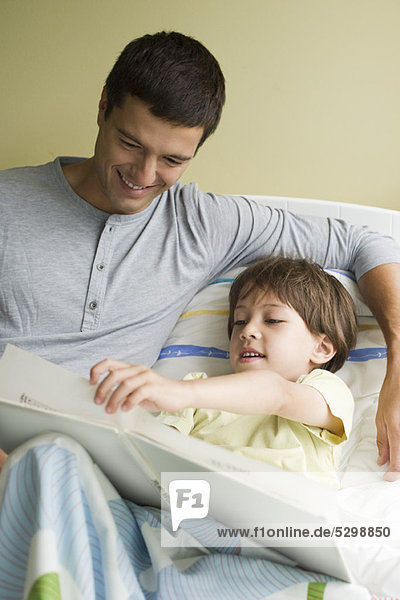 Father and son reading book together in bed