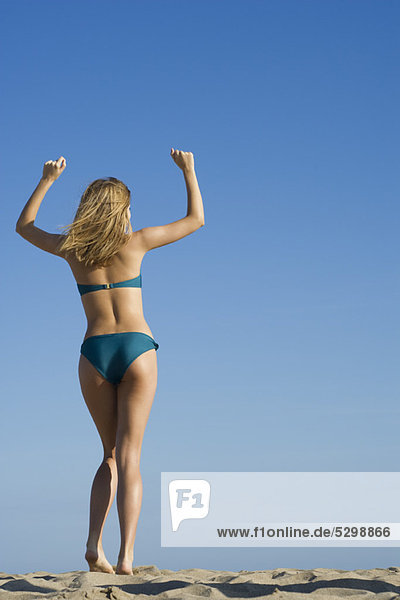 Woman at the beach with arms raised in air  rear view