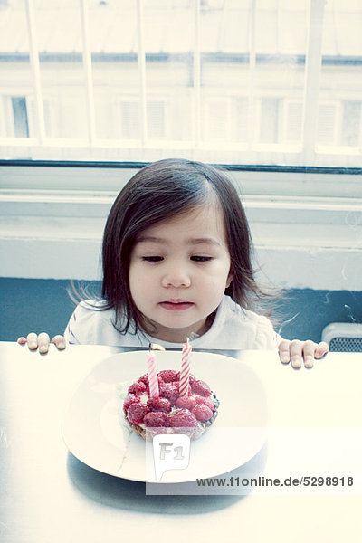 Kleines Mädchen beim Ausblasen von Kerzen auf Geburtstagskuchen