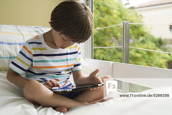 Junge auf dem Bett sitzend  mit digitalem Tablett