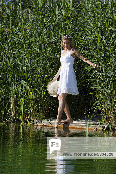 Frau steht auf einem Holzsteg am Wasser