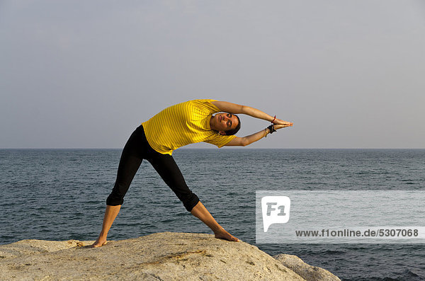 Woman in a yoga position  Trikonasana  by the sea in Kanyakumari  Tamil Nadu  India  Asia