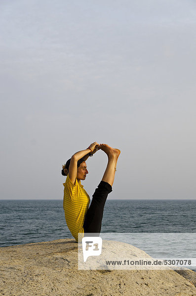 Woman in a yoga position  a variation of Paschimothanasana  by the sea in Kanyakumari  Tamil Nadu  India  Asia