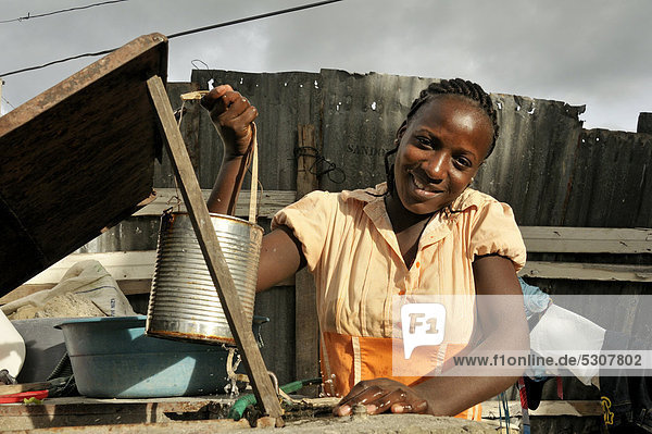 Junge dunkelhäutige Frau holt Wasser in einer Blechdose aus einem Brunnen  Port-au-Prince  Haiti  Karibik  Zentralamerika