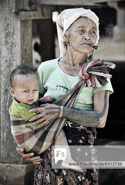 Rauchende Großmutter mit Enkel im Tragetuch in Dorf am Mekong  Laos  Südostasien  Asien