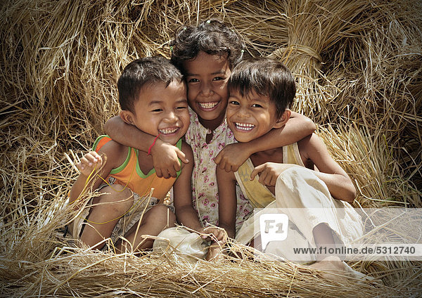 Three laughing children sitting on rice straw  Cambodia  Southeast Asia  Asia