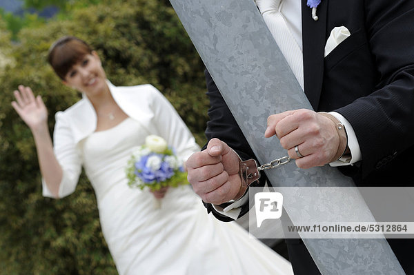 Bräutigam hängt mit Handschellen an Säule und die Braut winkt