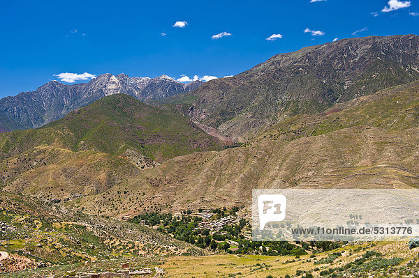 Berglandschaft im Hohen Atlas im Tal liegt eine kleine Siedlung der Berber umgeben von Bäumen Passstraße Tizi-n-Test Südmarokko Marokko Afrika