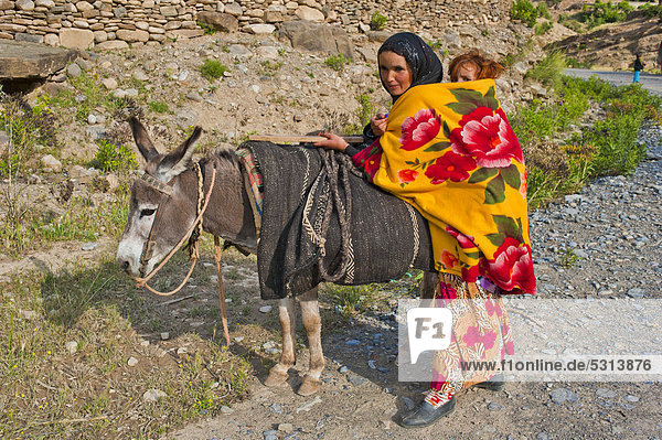 Eine junge Mutter ist unterwegs mit einem Esel und trägt ihr kleines Kind im Tragetuch auf dem Rücken  Hoher Atlas  Marokko  Afrika