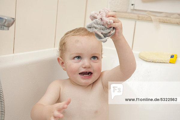 Junge  2 Jahre  spielt in der Badewanne mit einem Waschlappen