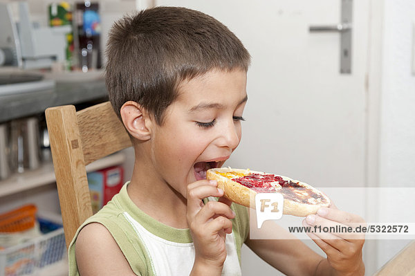 Junge  7 Jahre  beißt in ein mit verschiedenen Marmeladen bestrichenes Brötchen