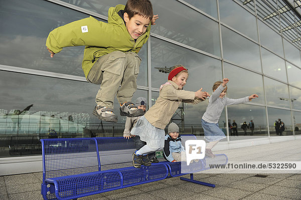 Kinder  3 bis 7 Jahre  springen zusammen von einer Bank am Flughafen herunter  Flughafen Frankfurt  Frankfurt am Main  Hessen  Deutschland  Europa