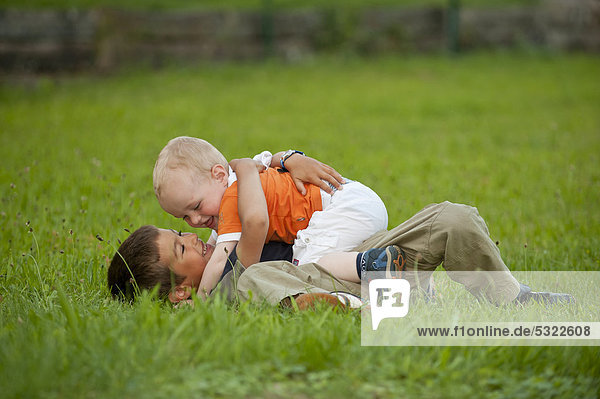 Junge  6 Jahre  spielt mit seinem kleinen Bruder  2 Jahre  auf einer Wiese